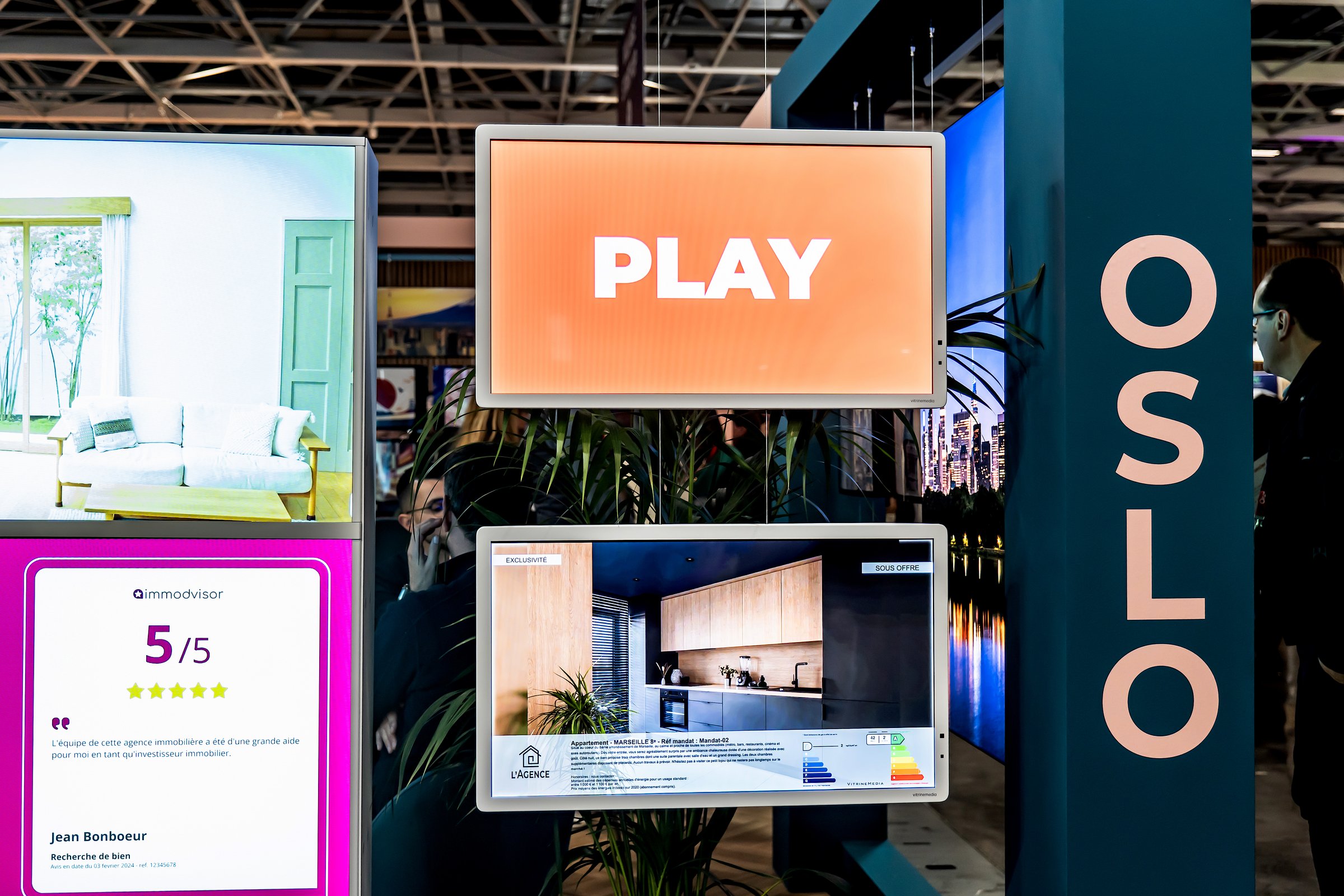 To liggende Light&Play-skærme hænger i wire i et butiksvindue og viser henholdsvis et kampagnemotiv og et interiørbillede.