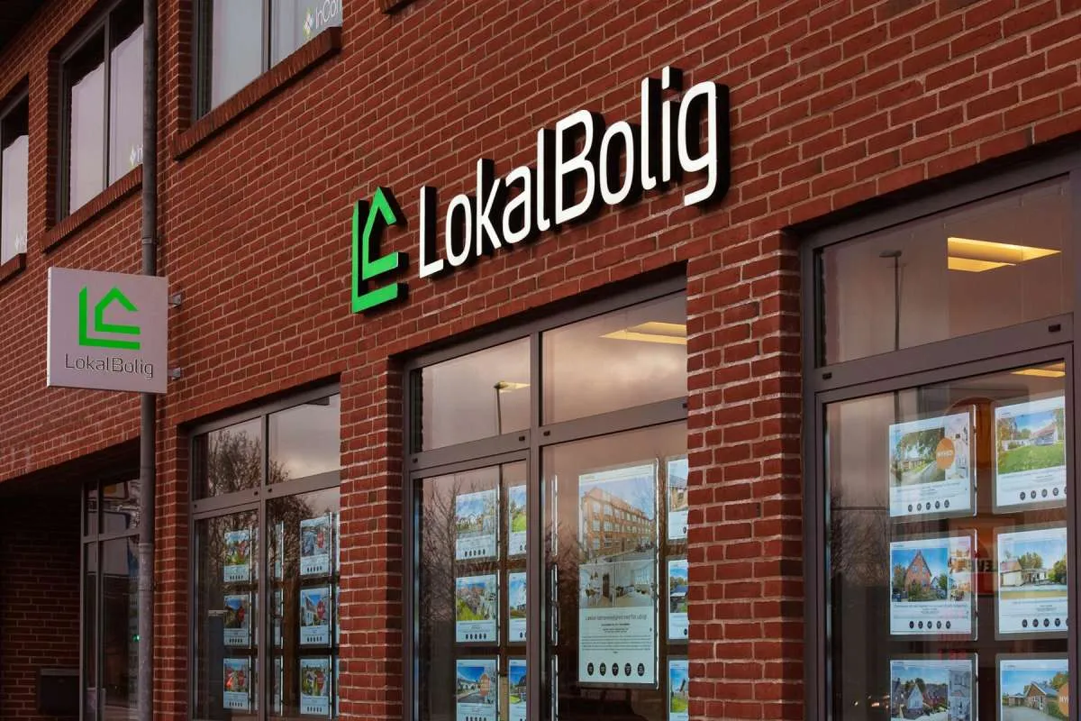 LokalBoligs butiksfacade i røde mursten med belyste A3-plakater i stående format i både vinduer og døroplukninger.